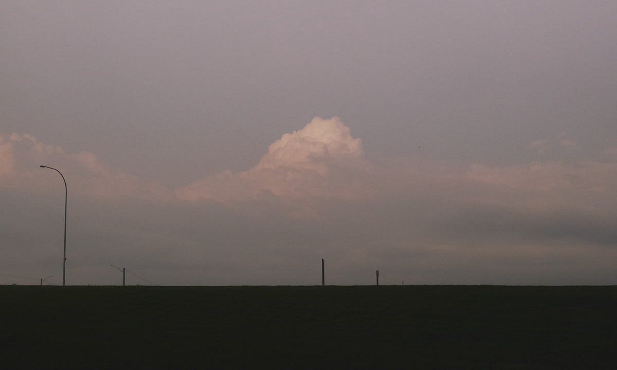 Silhouettes of street lamps against an evening sky, with a large cloud in the middle