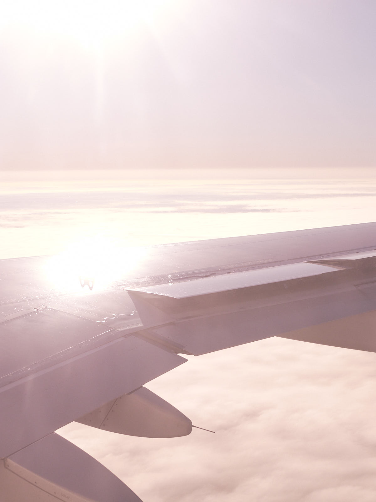 Hazy wing of a plane with sunshine reflecting on it, fading into the clouds